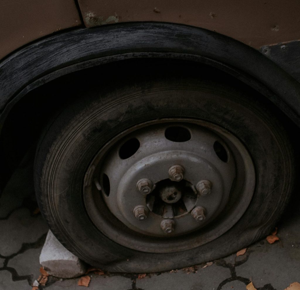Detailansicht eines platten Reifens an einem Auto, das im Freien auf einer befestigten Fläche geparkt ist.